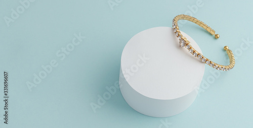 Fototapeta Diamond golden bracelet on white round platform on blue background with copy spa