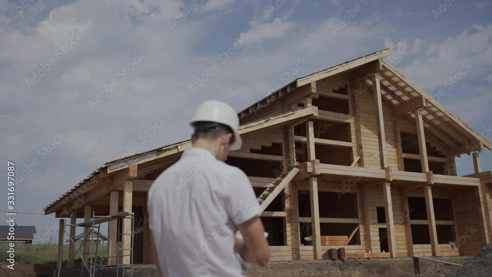 foreman Builder in helmet standing with his back to a wooden house foreman Builder in helmet standing with his back to a wooden house
