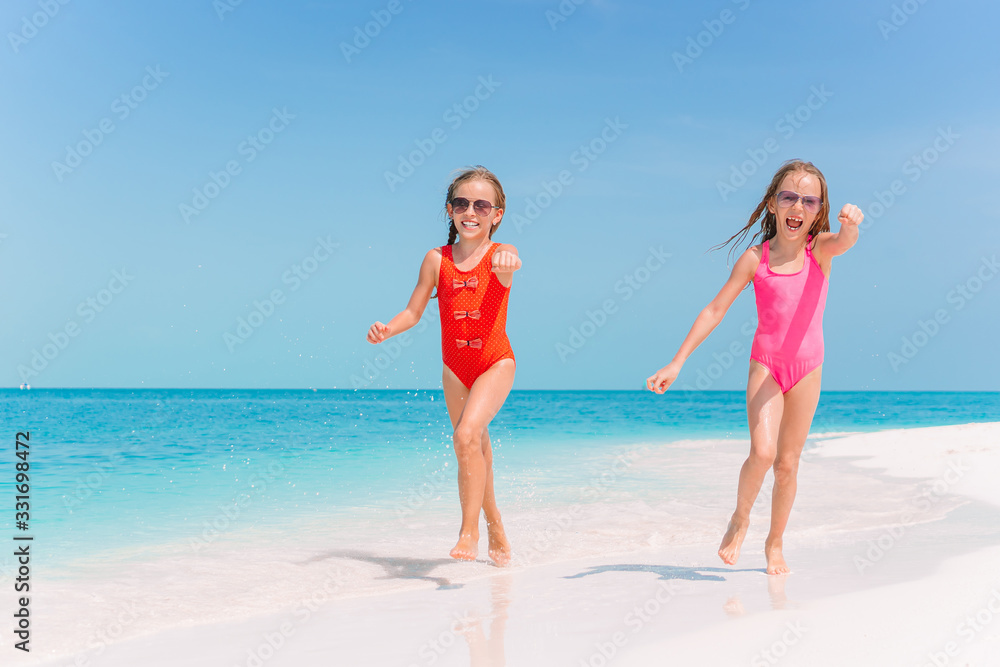 Little happy funny girls have a lot of fun at tropical beach playing together.