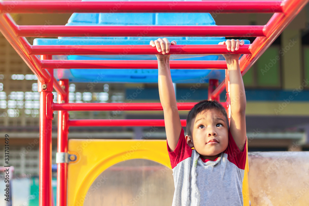 Fototapeta premium Kid exercise for health and sport concept. Happy Asian student​ child boy playing and hanging from a steel bar at the playground. 5-6 years old.