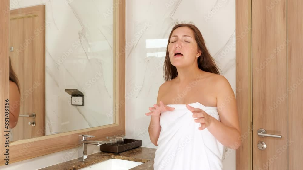 attractive brunette in white towel dances in stylish bathroom near large mirror and wooden door at home in morning attractive brunette in white towel dances in stylish bathroom near large mirror and wooden door at home in morning
