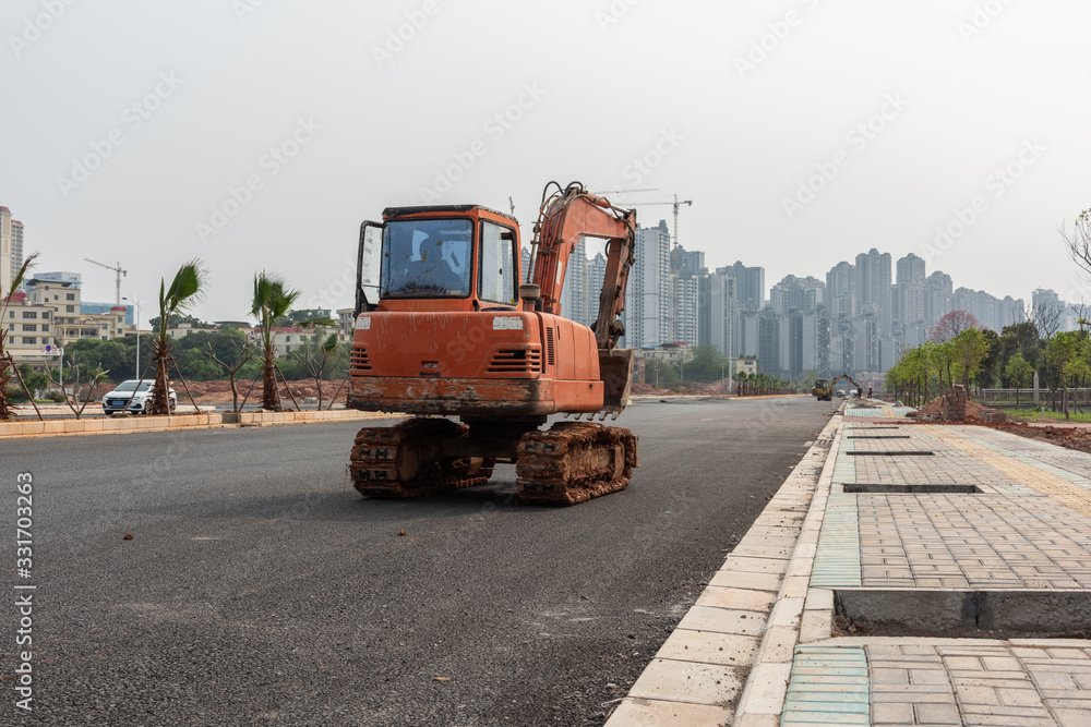 Excavator driving on asphalt road under construction in city