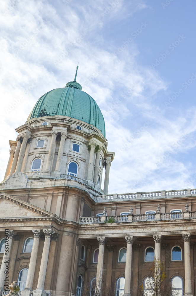 Fototapeta premium Buda Castle in Budapest, Hungary with light blue sky and clouds above. Historical castle and palace complex of the Hungarian kings. Facade with pillars, balconies and cupola. Vertical photo