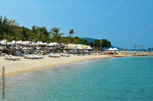 Fototapeta Naklejka Na Ścianę i Meble -  Sunbeds and umbrellas on a sandy beach with blue water in the tropics