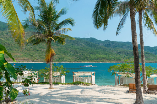 Beautiful palm trees and tents from the sun on a sandy beach and green mountains in the tropics