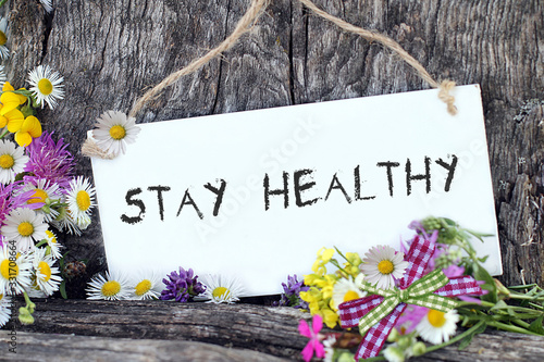 Stay Healthy als Schriftzug auf weisser Tafel mit Blumen in der Natur