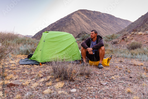 a man sits on a yellow bag near a tent in the mountains of Kyrgyzstan