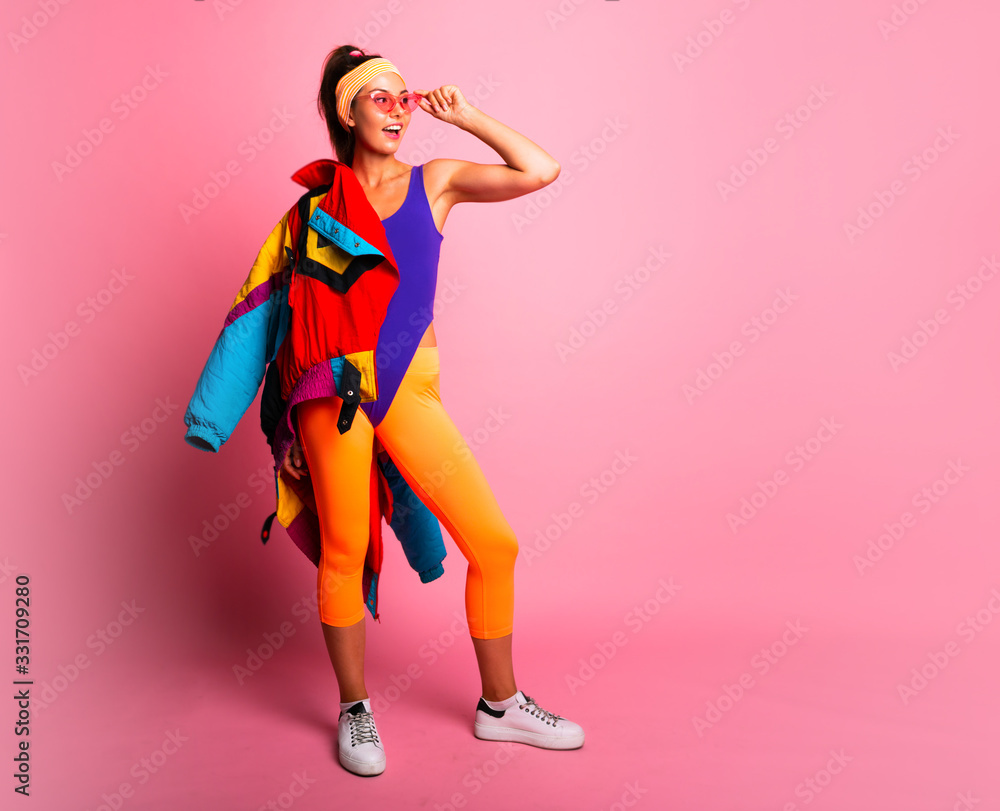Full length fashion portrait of young trendy woman in cap and jeans looking  away.young and cool, hipster girl with colored coat, orange leggings and  body suit. 80s 90s style Stock Photo