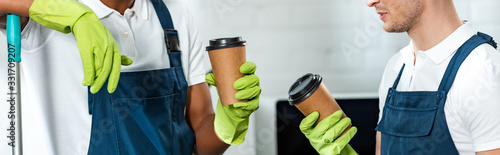 partial view of multicultural cleaners holding coffee to go in office, panoramic shot