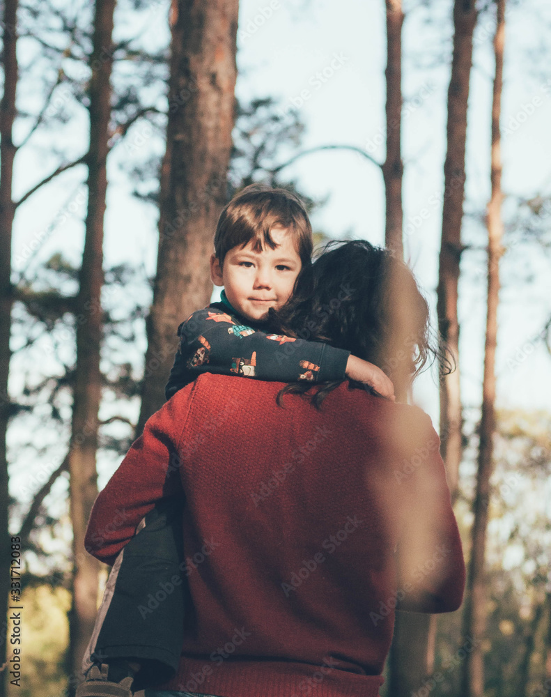 Obraz premium A baby peeks from under the back of mom in the forest