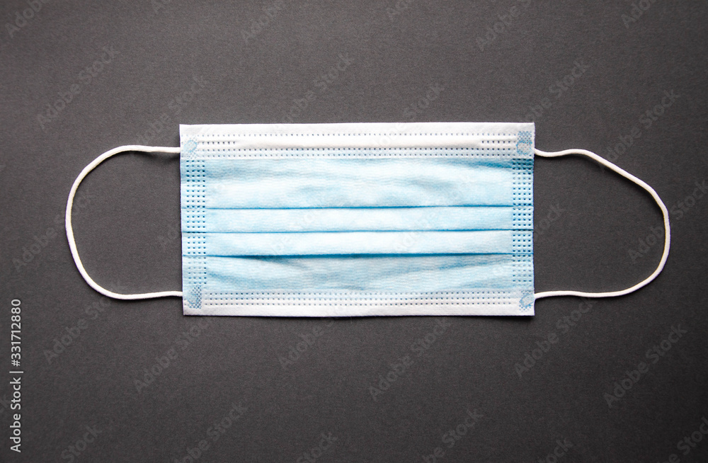 One blue medical masks lie on a gray background. Mast in open and closed state. Place for text. Copy Space. COVID-19 One blue medical masks lie on a gray background. Mast in open and closed state. Place for text. Copy Space. COVID-19