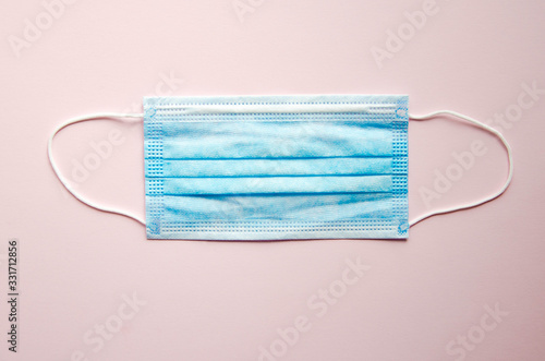 A blue medical mask lies alone on a pink background. Place for text. Copy Space. COVID-19
