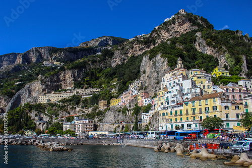 View of the city of Amalfi from the jetty with parked buses, the sea and the colorful houses on the slopes of the Amalfi coast in the province of Salerno, Campania, Italy. © romanadr