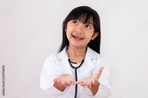 Asian child girl dressed in a doctor s uniform is carrying both hands with a smiling face on a white background.