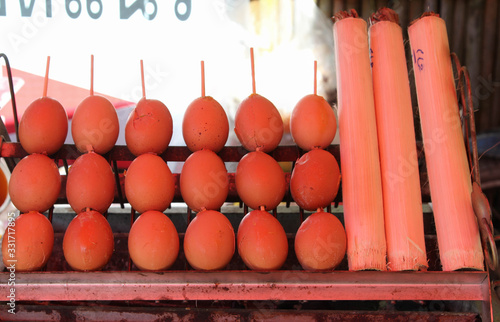 Grilled eggs skewers and khao lam on charcoal stove in the market.