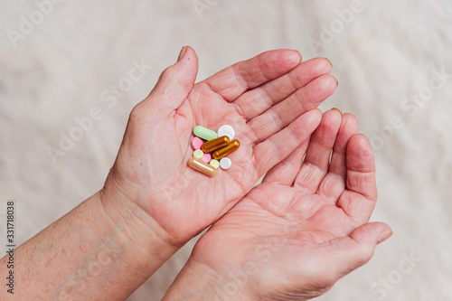 Many different pills in the hand of an elderly person.