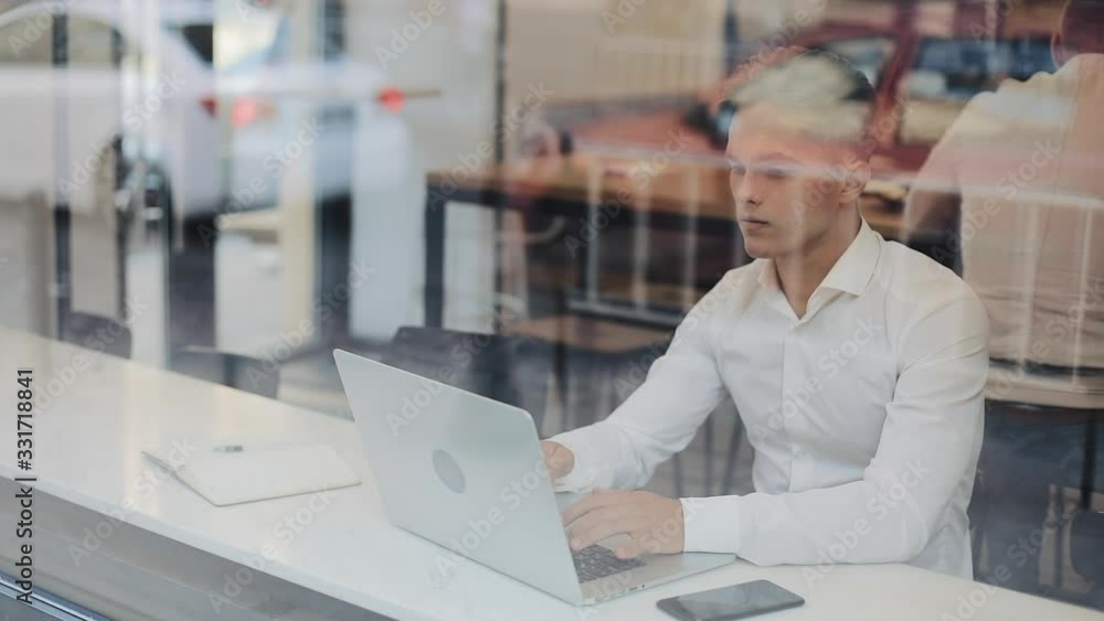 Tired young businessman sitting at a table in a cafe working on a laptop. Freelance, communication, IT, tired businessman concept Tired young businessman sitting at a table in a cafe working on a laptop. Freelance, communication, IT, tired businessman concept