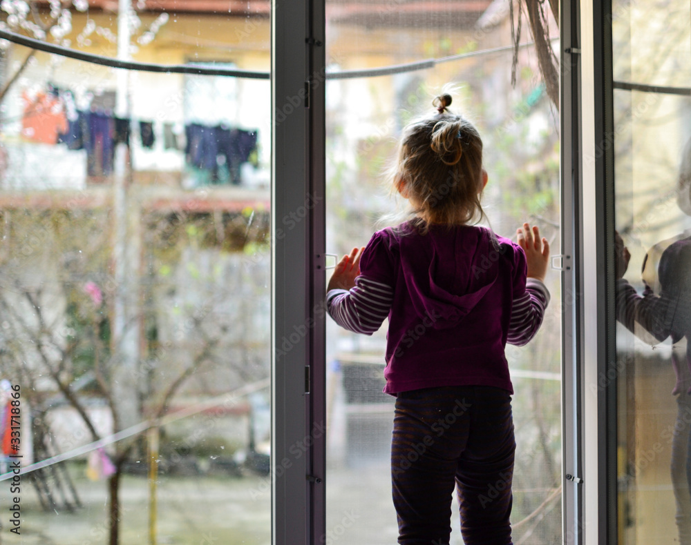 The child alone stands on the windowsill. Baby safety at home. Cute girl looks out the open window. - obrazy, fototapety, plakaty 