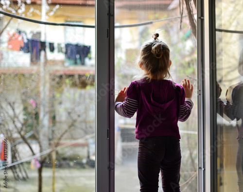 The child alone stands on the windowsill. Baby safety at home. Cute girl looks out the open window.