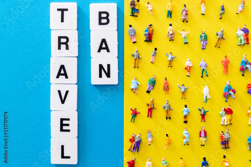Travel ban word on a blue background and a yellow background with aligned people miniatures. Concept for the stop of banned travel and tourism. Travel forbidden due to coronavirus pandemic worldwide