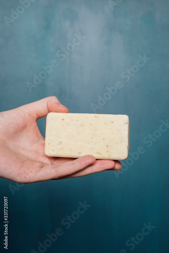 Female hand holds a piece of beige speckled soap on a blue background