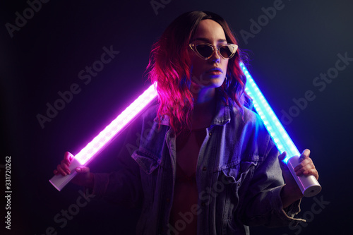 Portrait of young girl in glasses holding light sticks in red and blue neon in studio