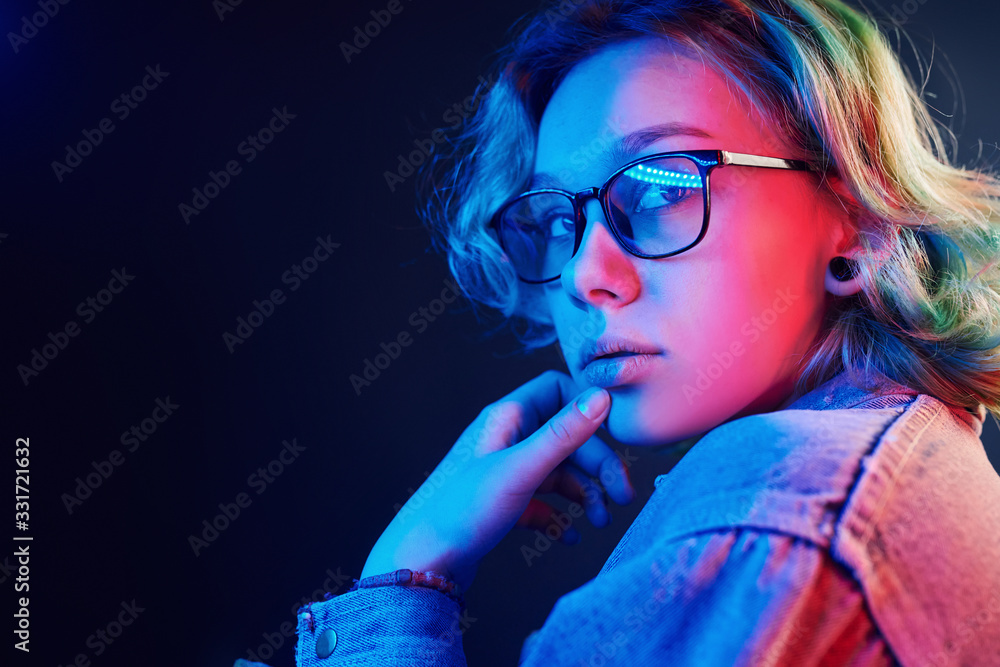 Portrait of young alternative girl in glasses with green hair in red and blue neon light in studio Portrait of young alternative girl in glasses with green hair in red and blue neon light in studio