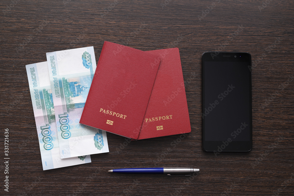 two passports, money, a smartphone and a fountain pen on a dark wooden table two passports, money, a smartphone and a fountain pen on a dark wooden table
