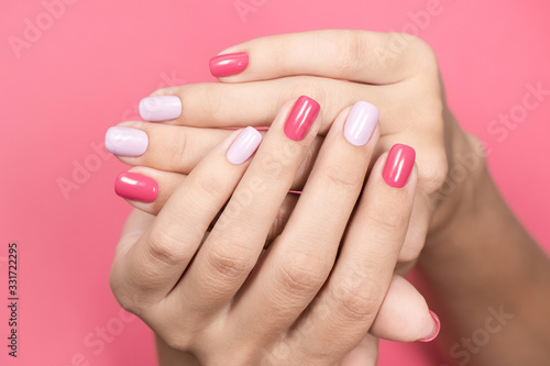 Closeup view photography of two crossed beautiful white hands of caucasian adult woman with trendy asymmetric two colours bright manicure isolated on pastel pink background. Beauty and fashion concept