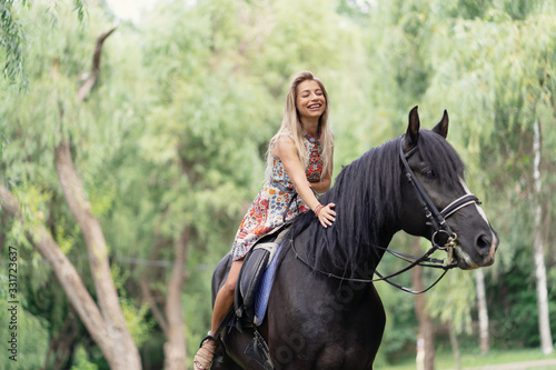 Young woman in a bright colorful dress riding a black horse