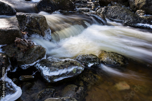 Brook of water in winter nature. Cold stream water flows between snowed stones. 