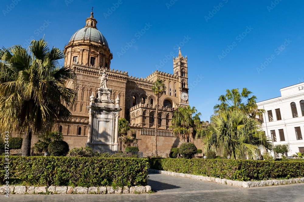 The bell tower with clock and cupola of Palermo Cathedral with palm trees in Sicily
