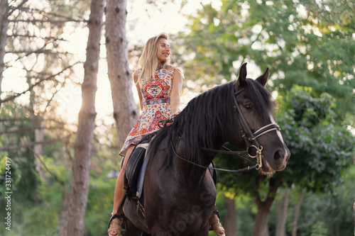 Young woman in a bright colorful dress riding a black horse © arthurhidden