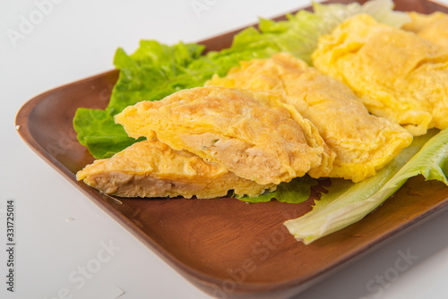 The eggs are wrapped in meat and lettuce is placed under them. They are packed in a wooden tray on a white background