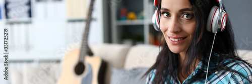 Portrait of smiling lady in modern headset playing synthesizer by notes. Lovely woman in stylish casual shirt looking at camera with happiness and tenderness. Art concept