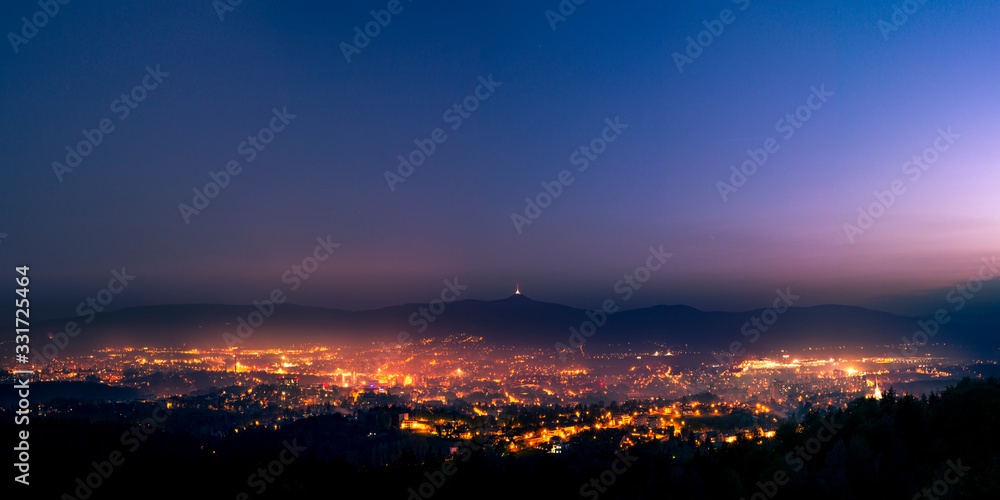 Shining town during dusk in the valley. Light fog flows above the town and disperse lights.