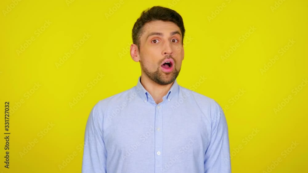 Young man in light blue shirt is surprised, opens his mouth and looks at camera. Yellow background with copy space. Human emotions. 4k footage Young man in light blue shirt is surprised, opens his mouth and looks at camera. Yellow background with copy space. Human emotions. 4k footage