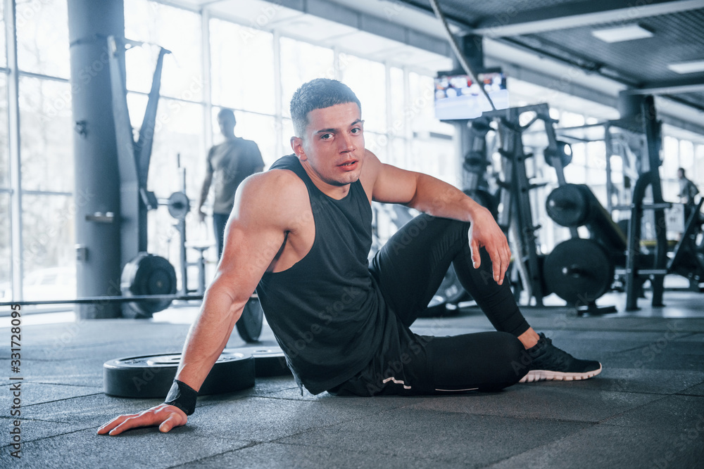 Strong young man in sportive clothes have fitness day in the gym, sitting and taking a break Strong young man in sportive clothes have fitness day in the gym, sitting and taking a break