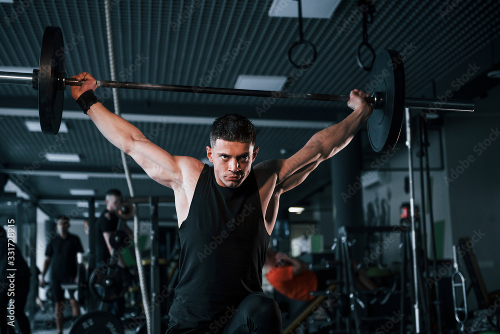 Strong young man in sportive clothes doing exercises with heavy weights in the gym Strong young man in sportive clothes doing exercises with heavy weights in the gym