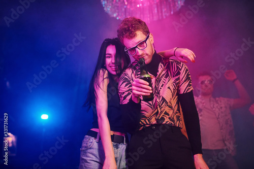 Guy in glasses drinks beer. Young people is having fun in night club with colorful laser lights