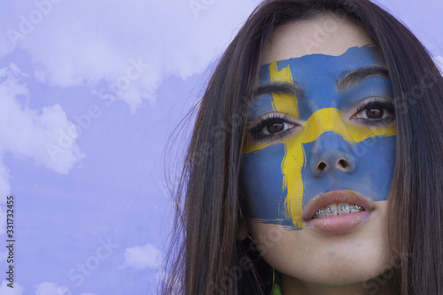 Flag of Sweden painted on a face of a smiling swedish young woman. Copyspace.