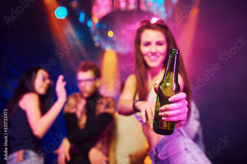 Girl holding bottle. Young people is having fun in night club with colorful laser lights