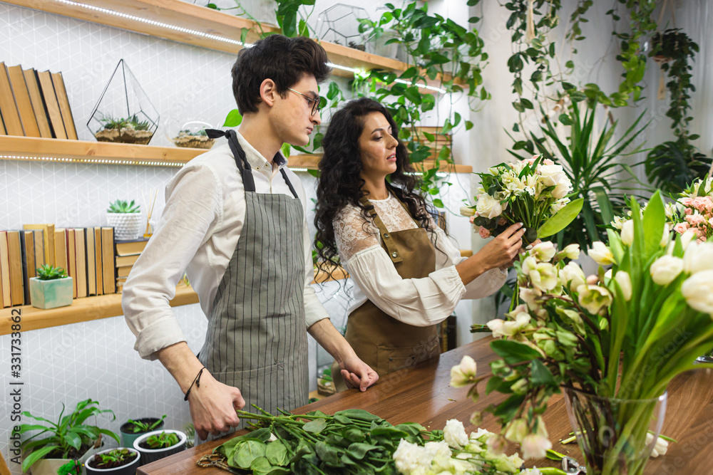 Obraz premium Attractive young male florist with glasses and apron is training at a flower shop