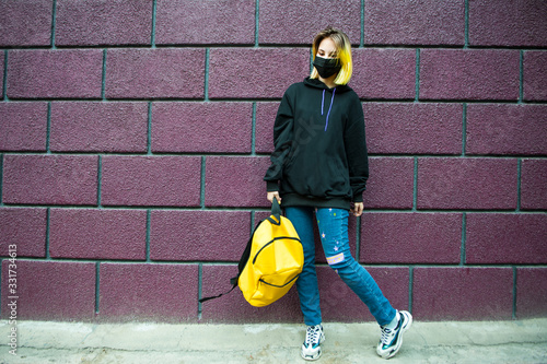 Teenager with yellow hair and backpack stand in front of brick wall