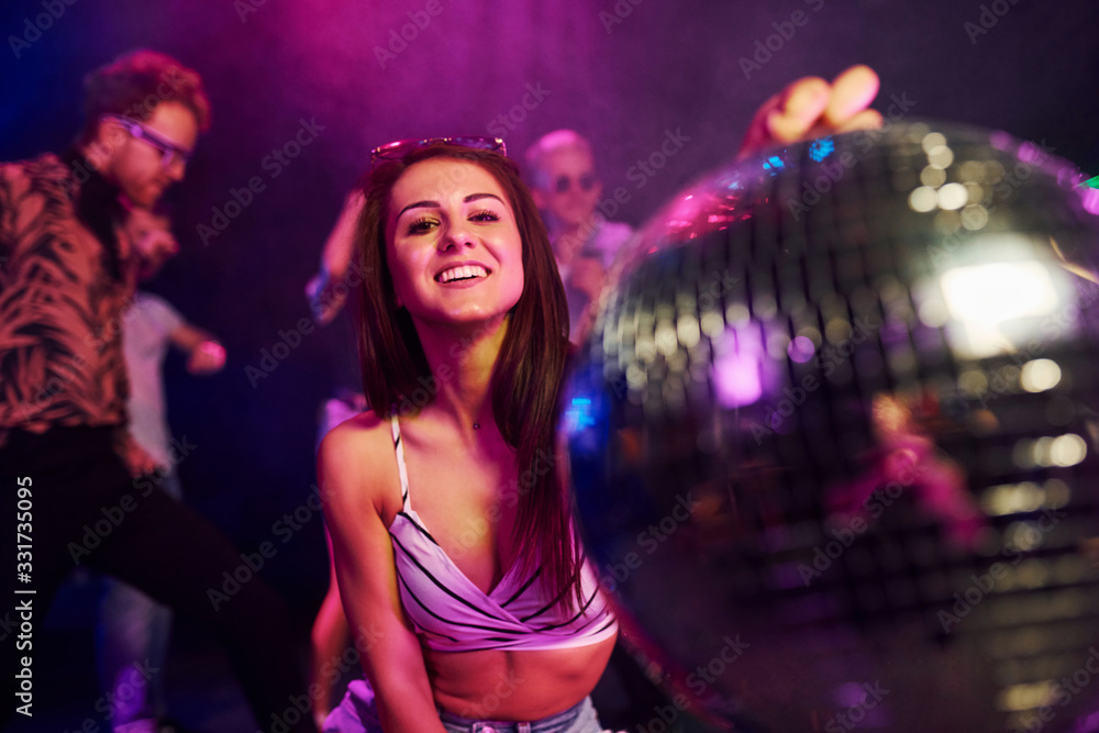 Girl sitting inside of night club with party ball in hands