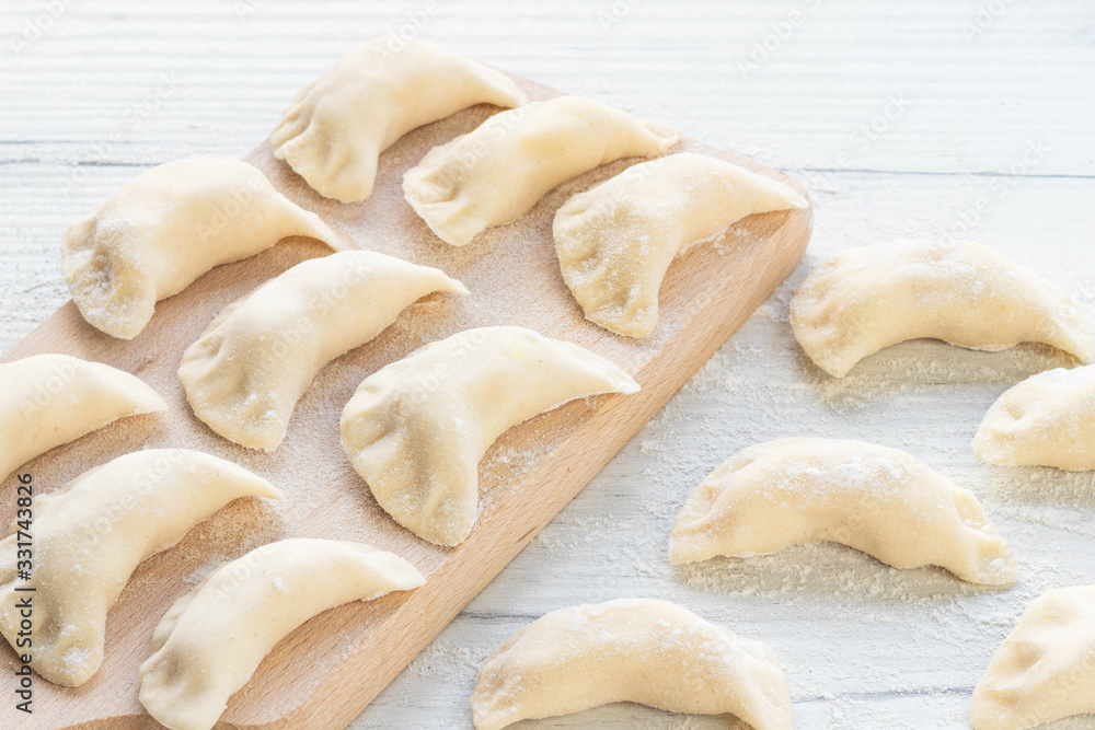 Cooking dumplings on a light background. Dumplings with potatoes on a wooden board. Cooking dumplings on a light background. Dumplings with potatoes on a wooden board.