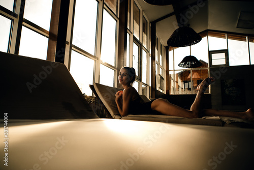 skinny caucasian girl laying on a deck chair in an indoor swimming pool in the sunset