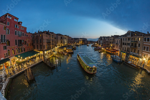 VENICE  ITALY - August 02  2019  View from Rialto Bridge in Venice at sunset time. Venetian Grand Canal with historical buildings  hotels  tourist boats  piles  berths. Fish eye lens shot