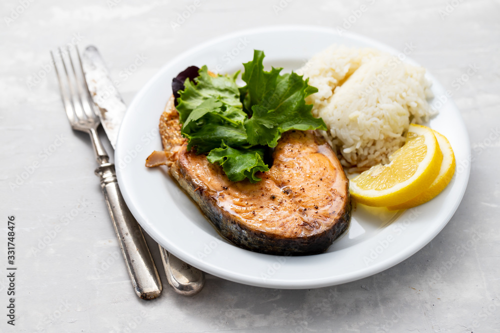 fried salmon with boiled rice, salad and lemon on white plate