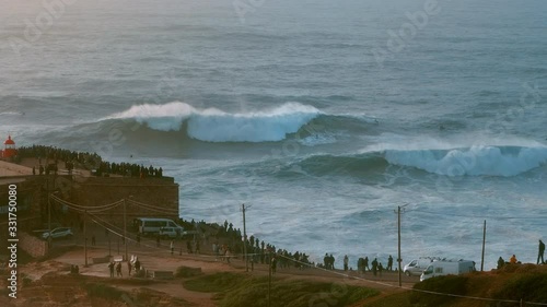 NAZARE, PORTUGAL - DECEMBER 22, 2019:  Amazing shot of a jetski pushing a big wave surfer to ride a massive wave in Nazare, Portugal. People are watching dangerous surfing: a popular tourist destinati photo